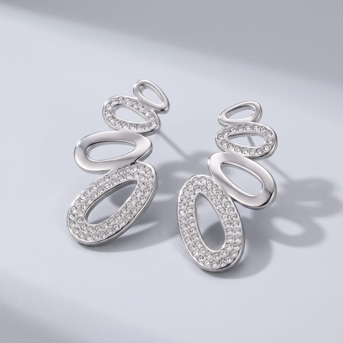 Agathe pavé oval silver earrings on a smooth gray surface cast soft directional shadows