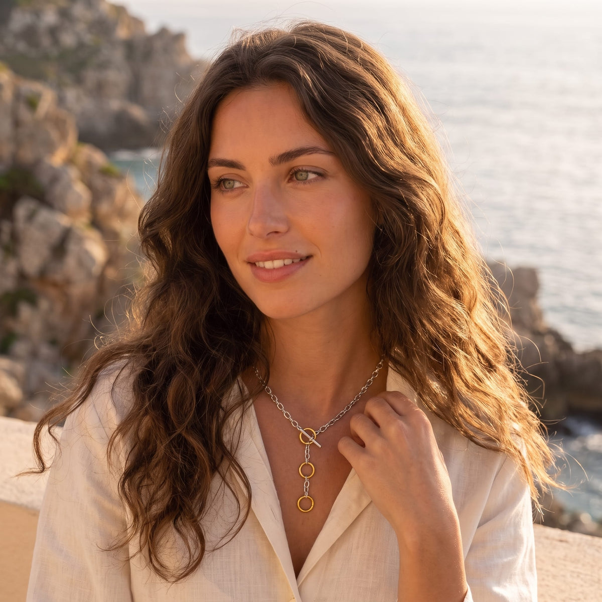 Woman wearing the Albane circle toggle two-tone necklace at the collarbone outdoors near the ocean