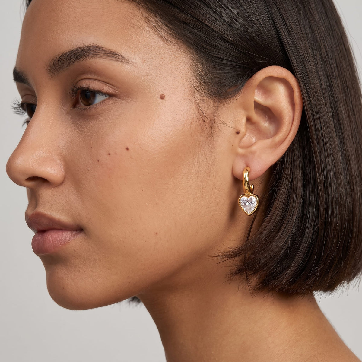 Woman wearing the Amandine hammered heart gold earrings on her ear with short hair