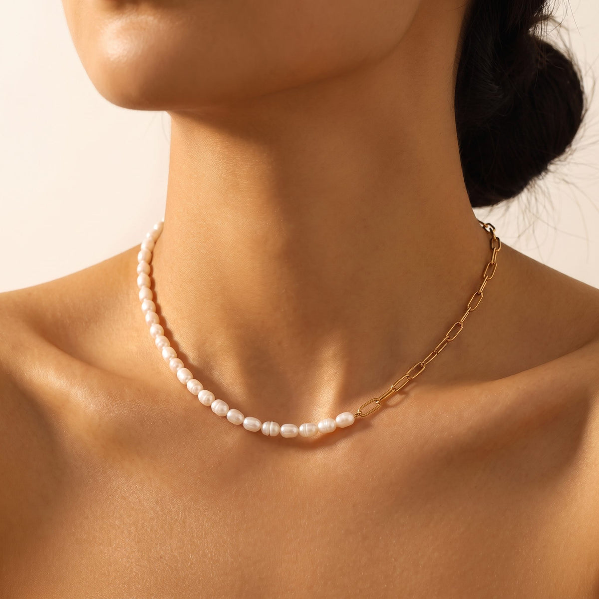 Close-up of a woman wearing the Amélie pearl paperclip gold necklace at the base of her neck