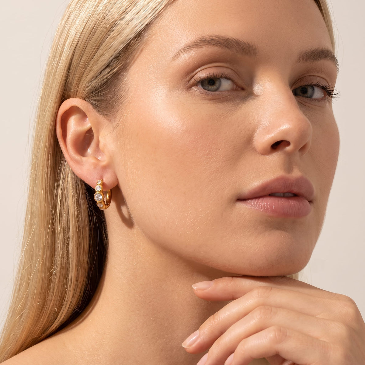 Woman wearing the Anaïs crystal huggie gold earrings on her earlobe with her hand resting under her chin
