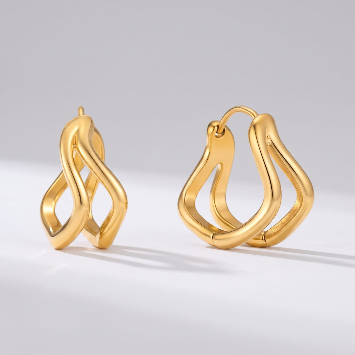 Anouk double wave gold earrings on a plain white surface casting subtle shadows