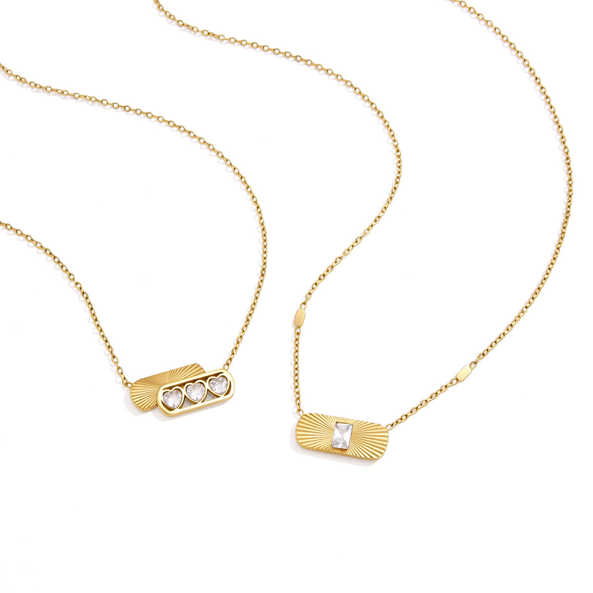 Aurora fluted sunburst tag with an emerald-cut crystal next to a heart trio necklace on white