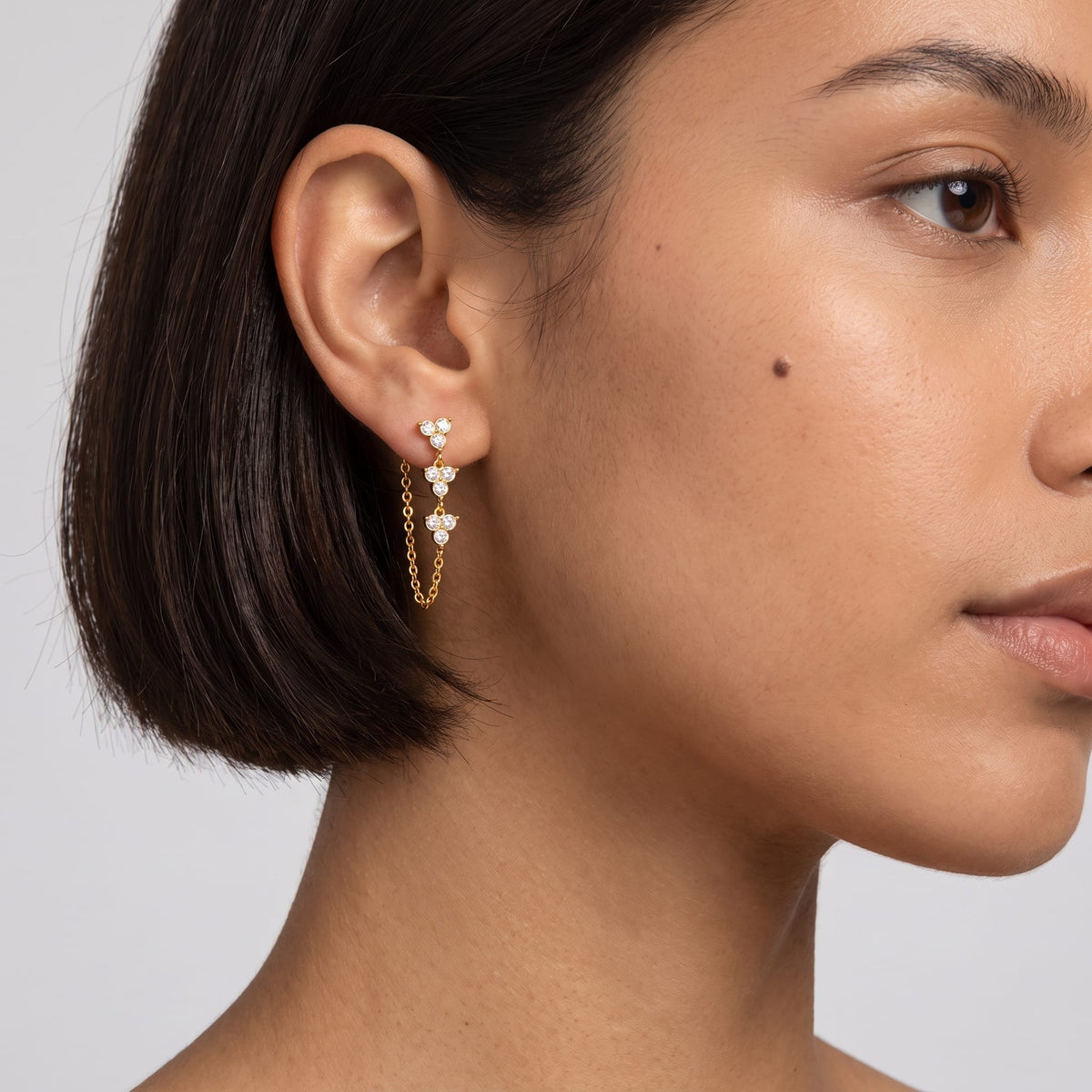 Woman wearing the Bettina crystal cascade gold earrings on her ear with short dark hair