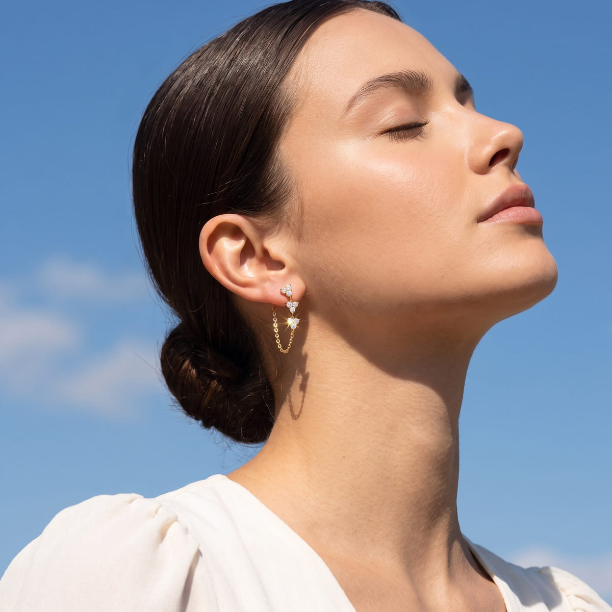 Woman wearing the Bettina crystal cascade gold earrings on her ear facing up toward blue sky