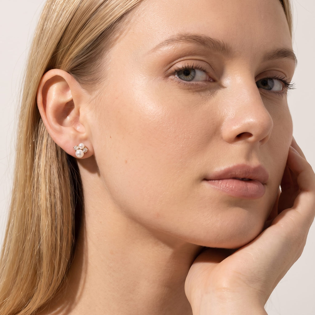 Woman wearing the Blanche pearl cluster gold earrings on her ear while resting her hand on her chin