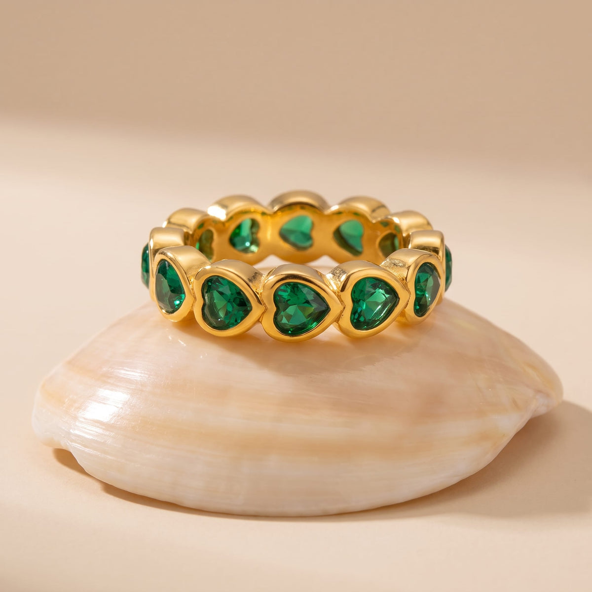 Camille green heart gold ring on a seashell against a beige background