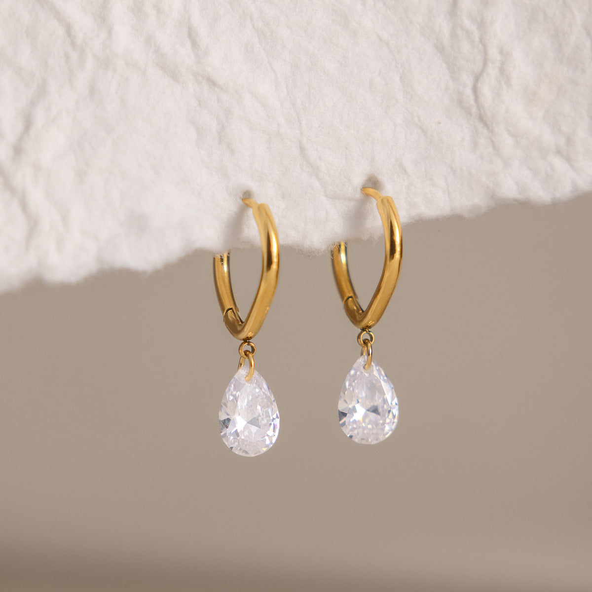 Pair of Carla teardrop huggies hanging from the edge of white handmade paper