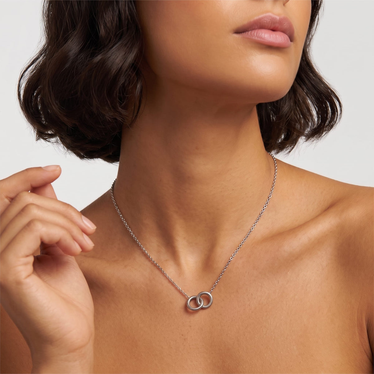 Woman wearing the Colette interlocking rings silver necklace at the collarbone, holding her hand near her face