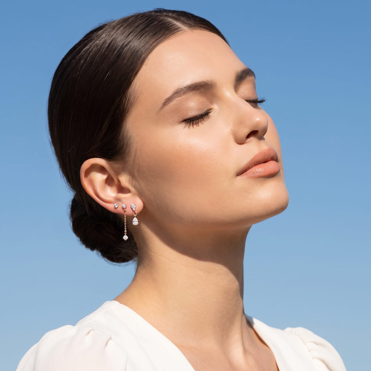 Woman wearing the Delfina drop trio gold earrings on the ear against a blue sky