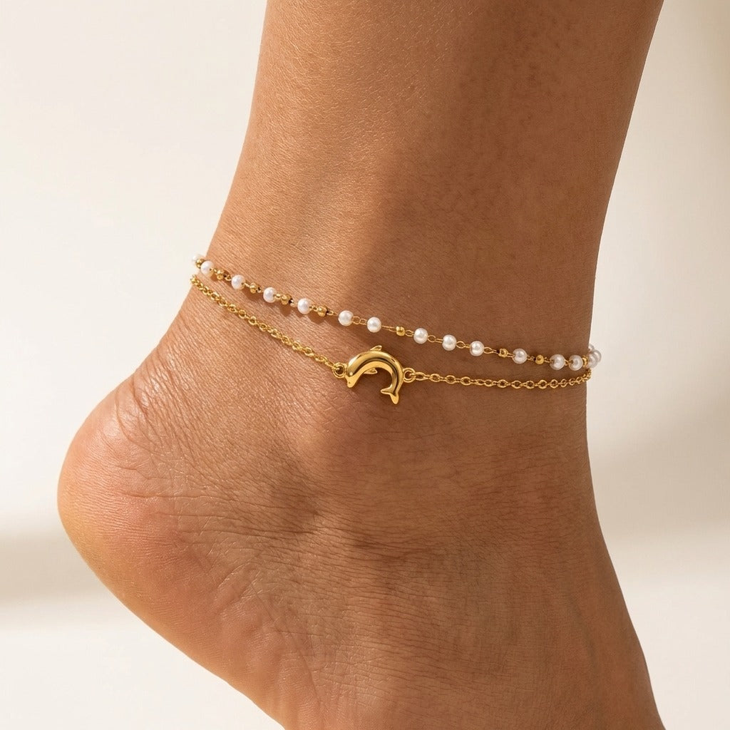 Chiara Delfino anklet on the ankle, a gold dolphin charm below a strand of small white pearls