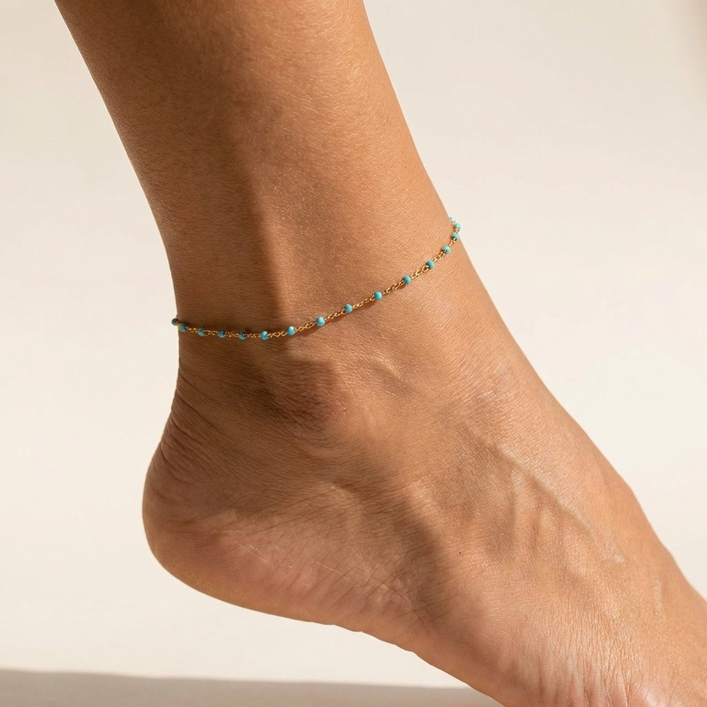 Woman wearing the Capri gold chain anklet dotted with small turquoise beads