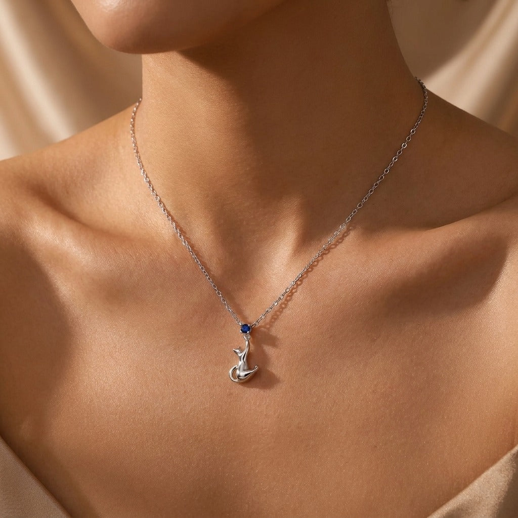 Woman wearing the Amélie silver kitten necklace, cat pendant with a blue stone at the collarbone