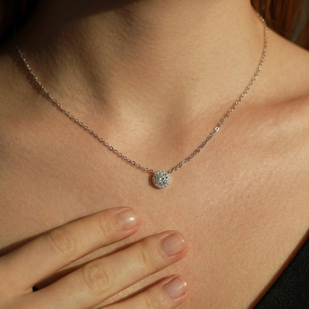 Woman with her hand below the Olivia Cercle silver necklace, a round crystal halo pendant at the collarbone