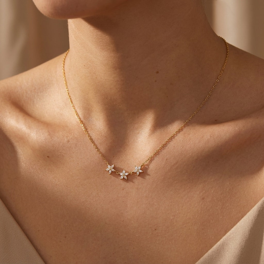 Woman wearing the Maia gold necklace with three linked crystal flowers at the collarbone