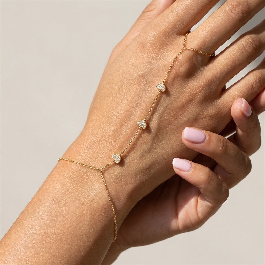 Woman wearing the Amélie gold hand chain with three crystal hearts running to a finger ring