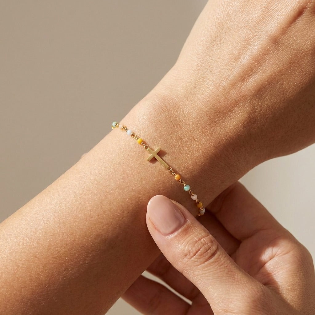 Woman wearing the Amélie Cross Bead bracelet in gold, a sideways cross between tiny colored beads