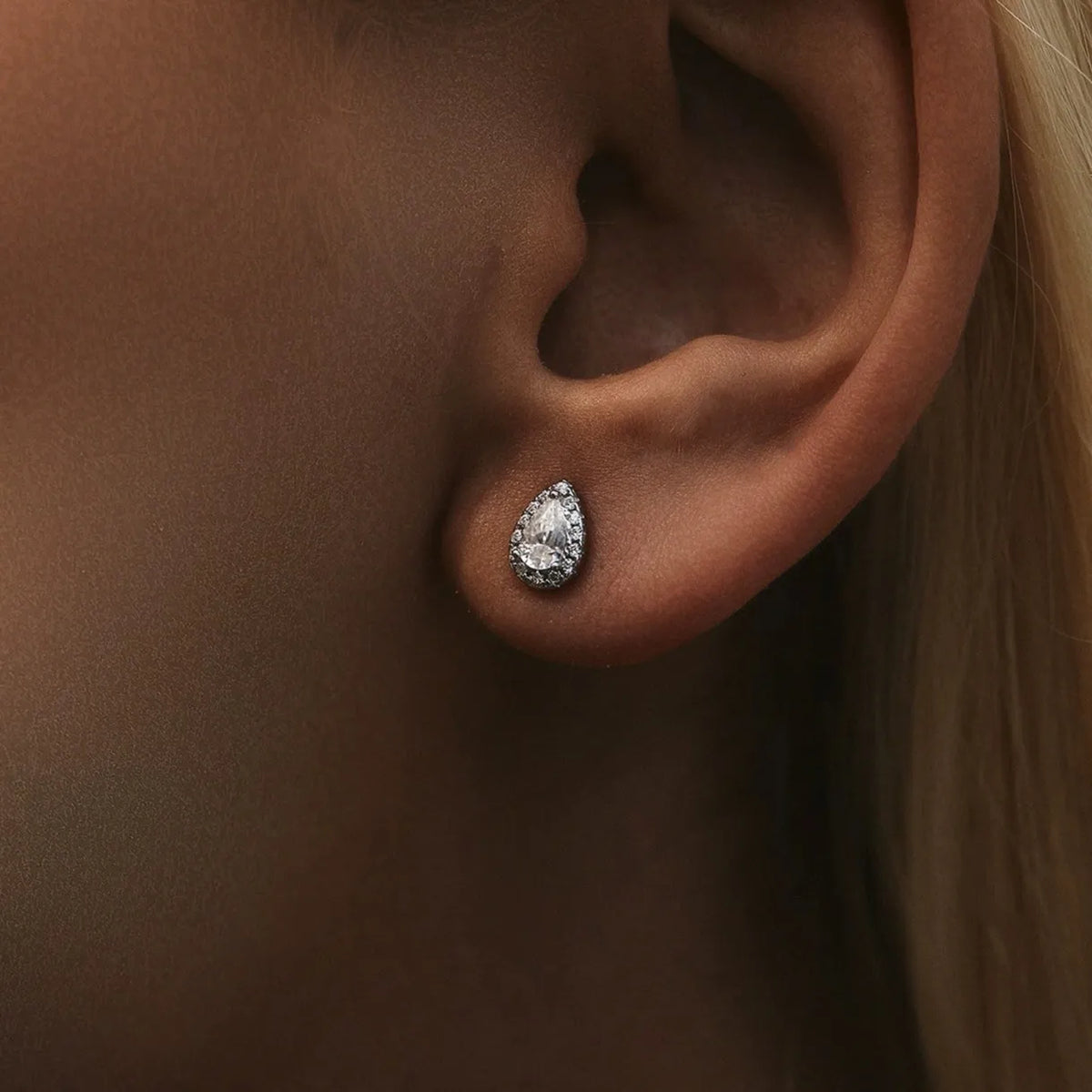 Close view of the Olivia Goutte silver stud on the ear, a pear-shaped crystal framed by a halo