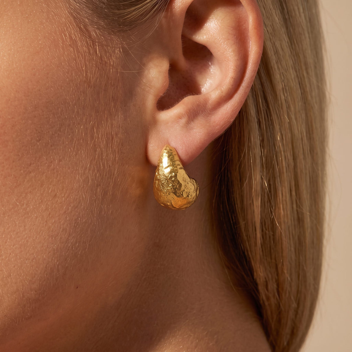 Woman wearing the Éden sculpted gold teardrop earring with a hammered texture