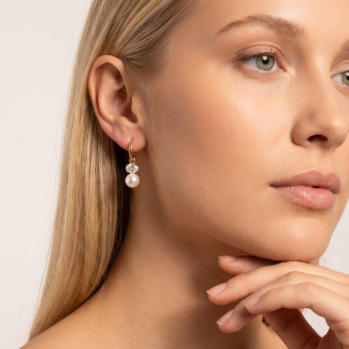 Woman wearing the Eléonore pearl drop gold earrings on the ear posing with hand