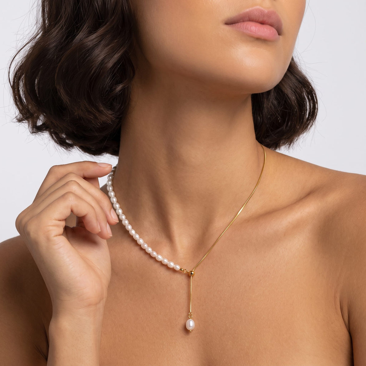 Woman with a dark bob wearing the Élise pearl lariat gold necklace, one hand raised near her neck