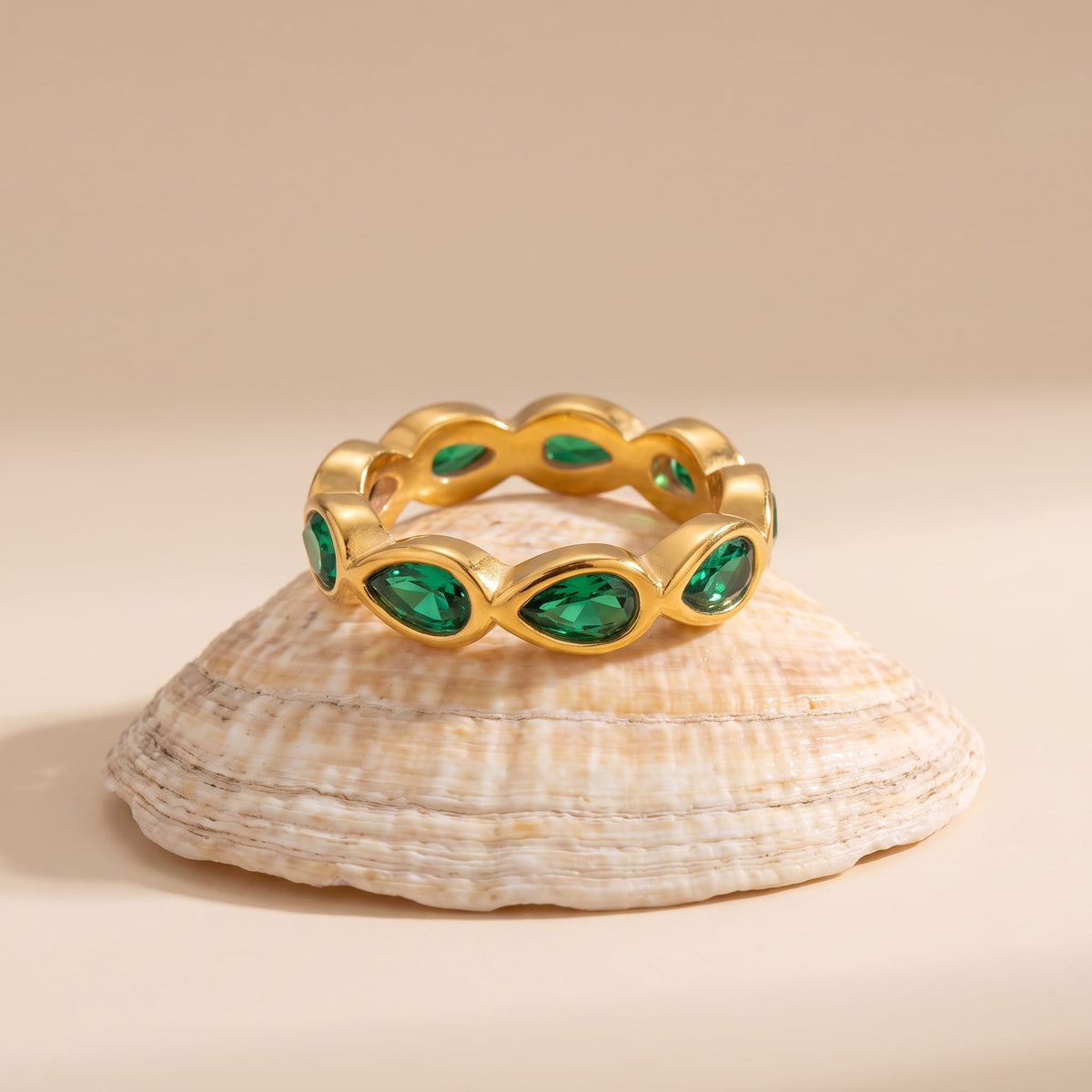 Élodie green pear gold ring on a textured seashell resting on a neutral background