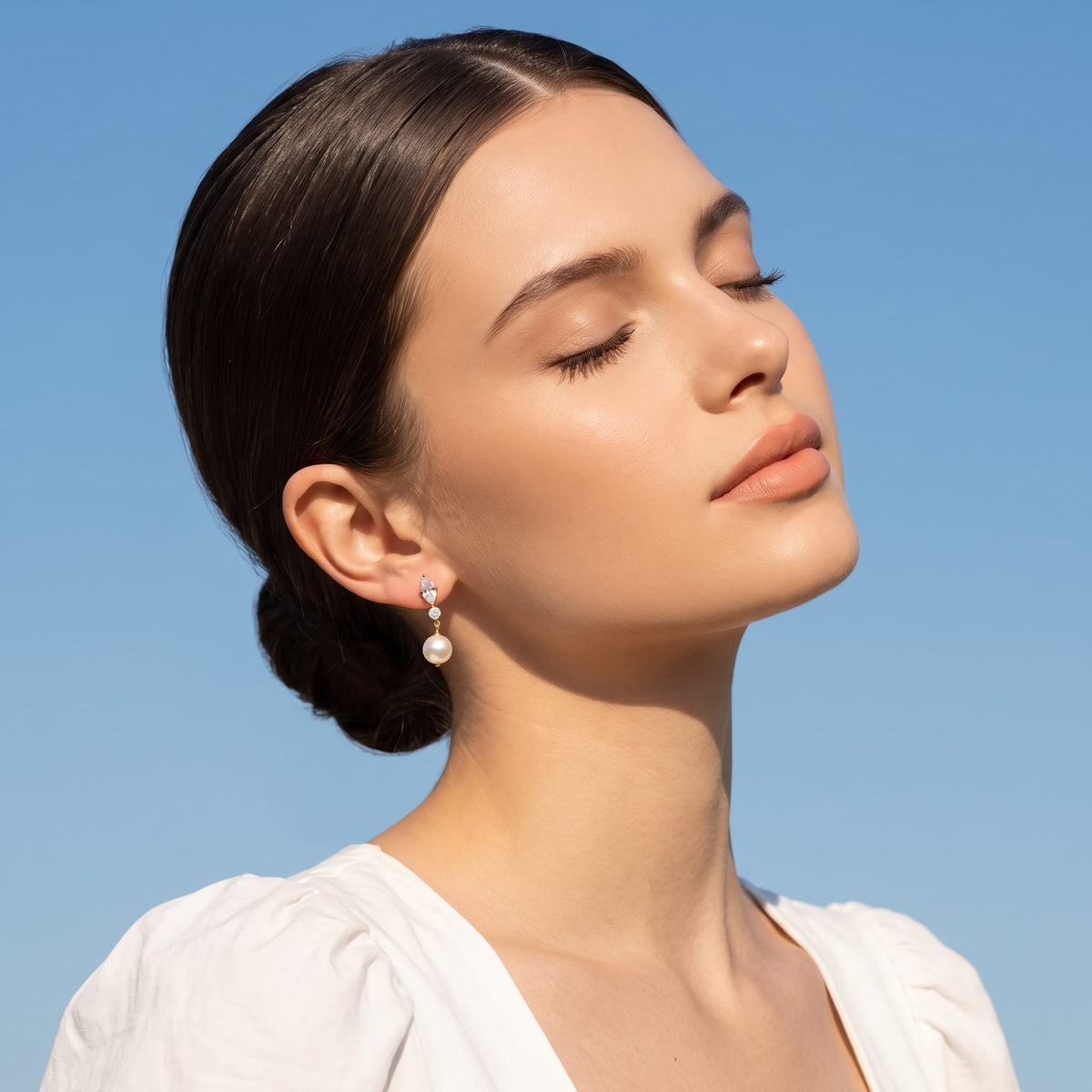 Woman wearing the Emilia marquise pearl gold earrings on her ear against blue sky background
