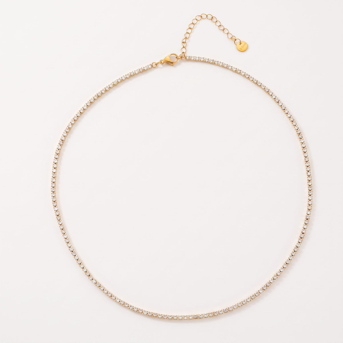 The Emma tennis chain gold necklace laid flat on an off-white surface