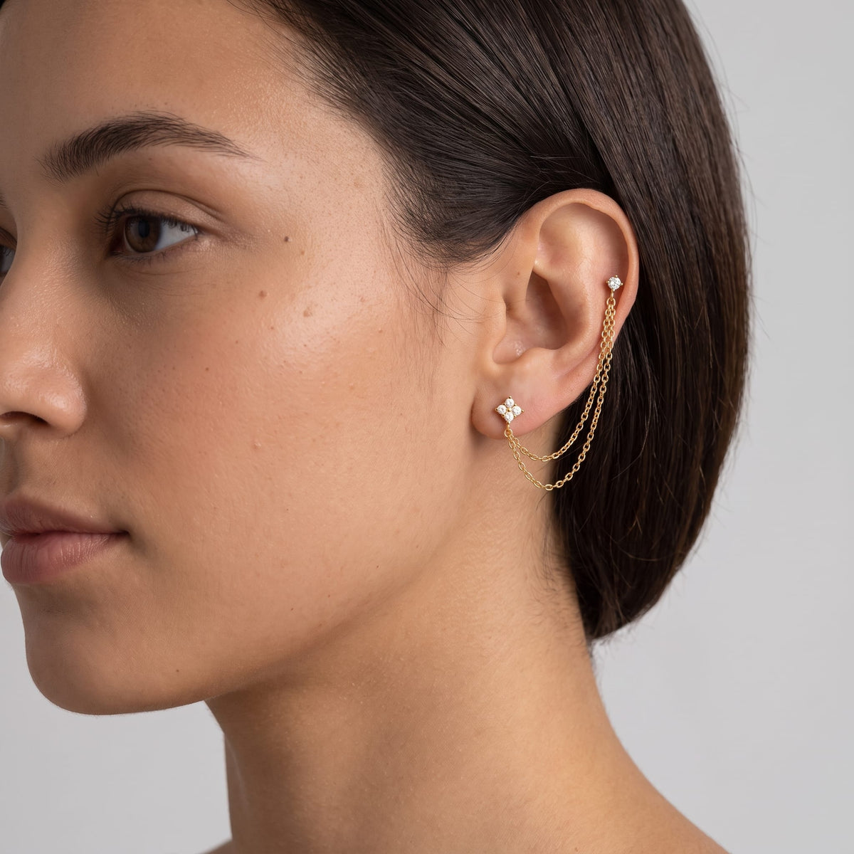 Woman wearing the Félicie flower chain gold earrings on her ear turned to the side