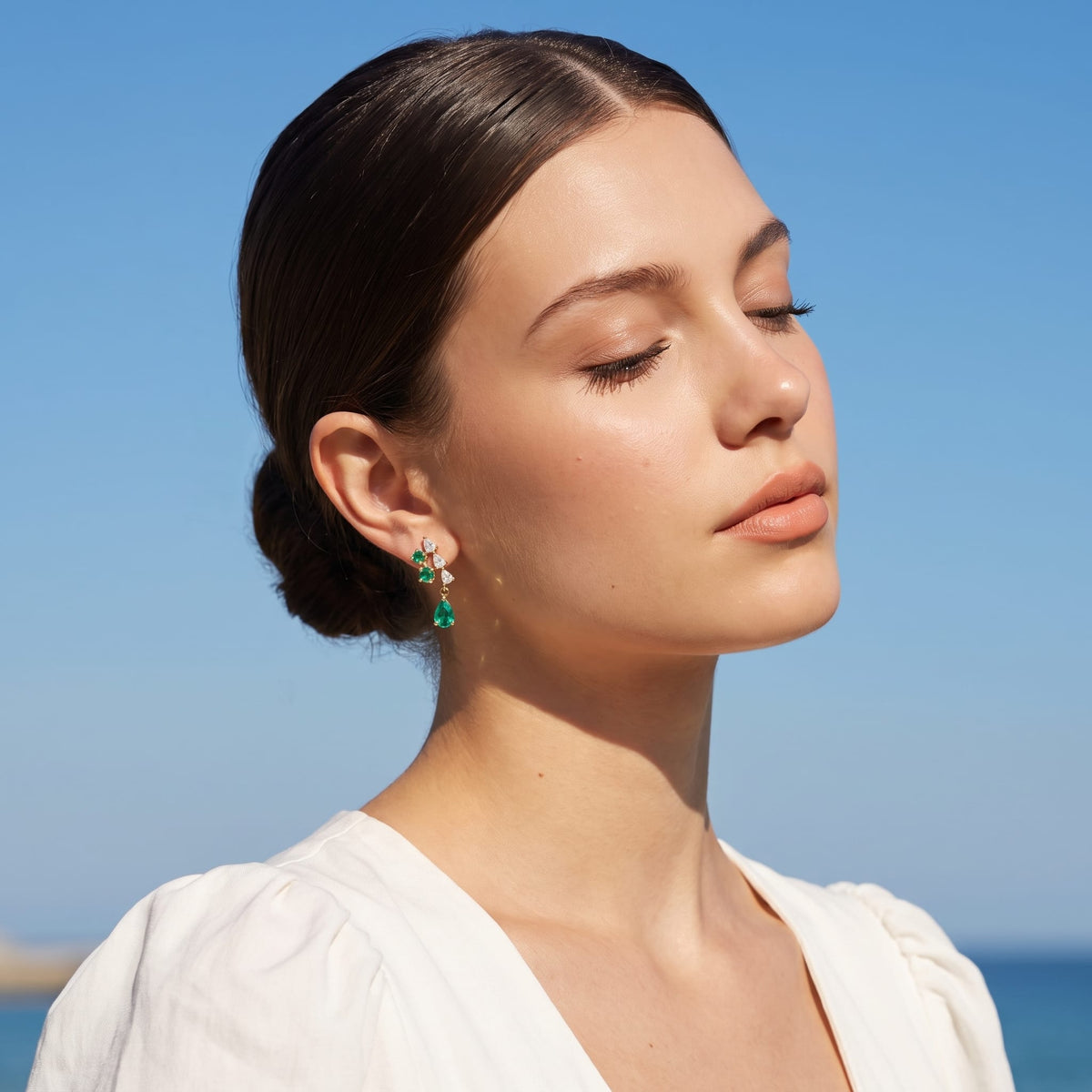 Woman wearing the Florentine green cascade gold earrings on her ear against a bright blue sky