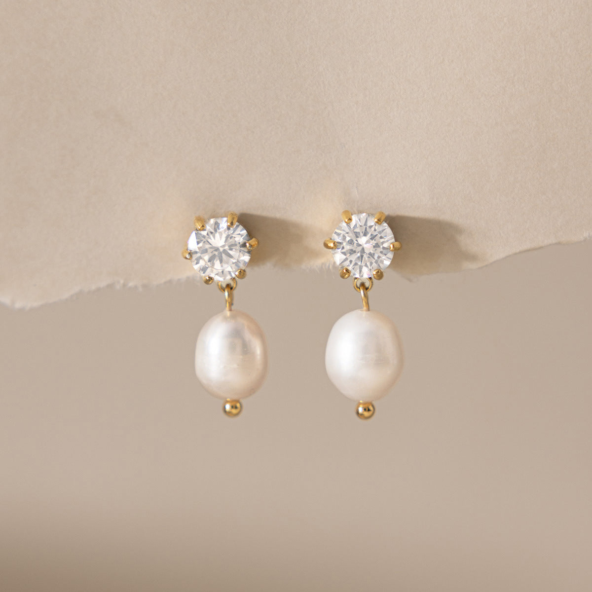 Ginevra crystal stud and pearl drop earrings pinned to torn beige paper