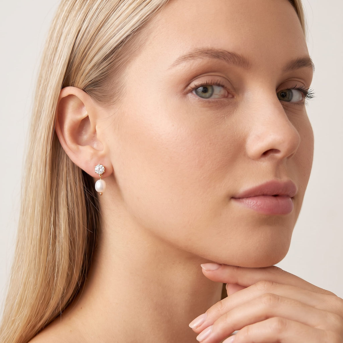 Woman wearing the Ginevra pearl drop gold earrings on the ear with hand under chin