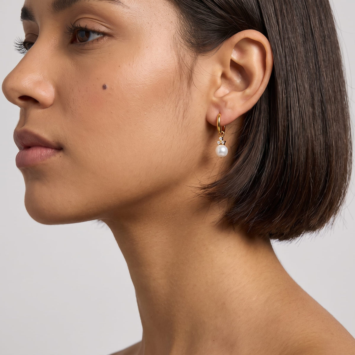 Woman wearing the Hortense pearl huggie gold earrings on her ear with short dark hair