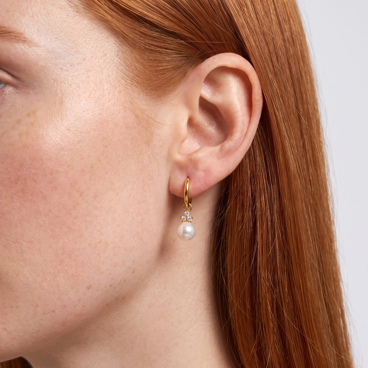 Wider view of a woman wearing the Hortense pearl huggie gold earrings on her ear in a close up shot