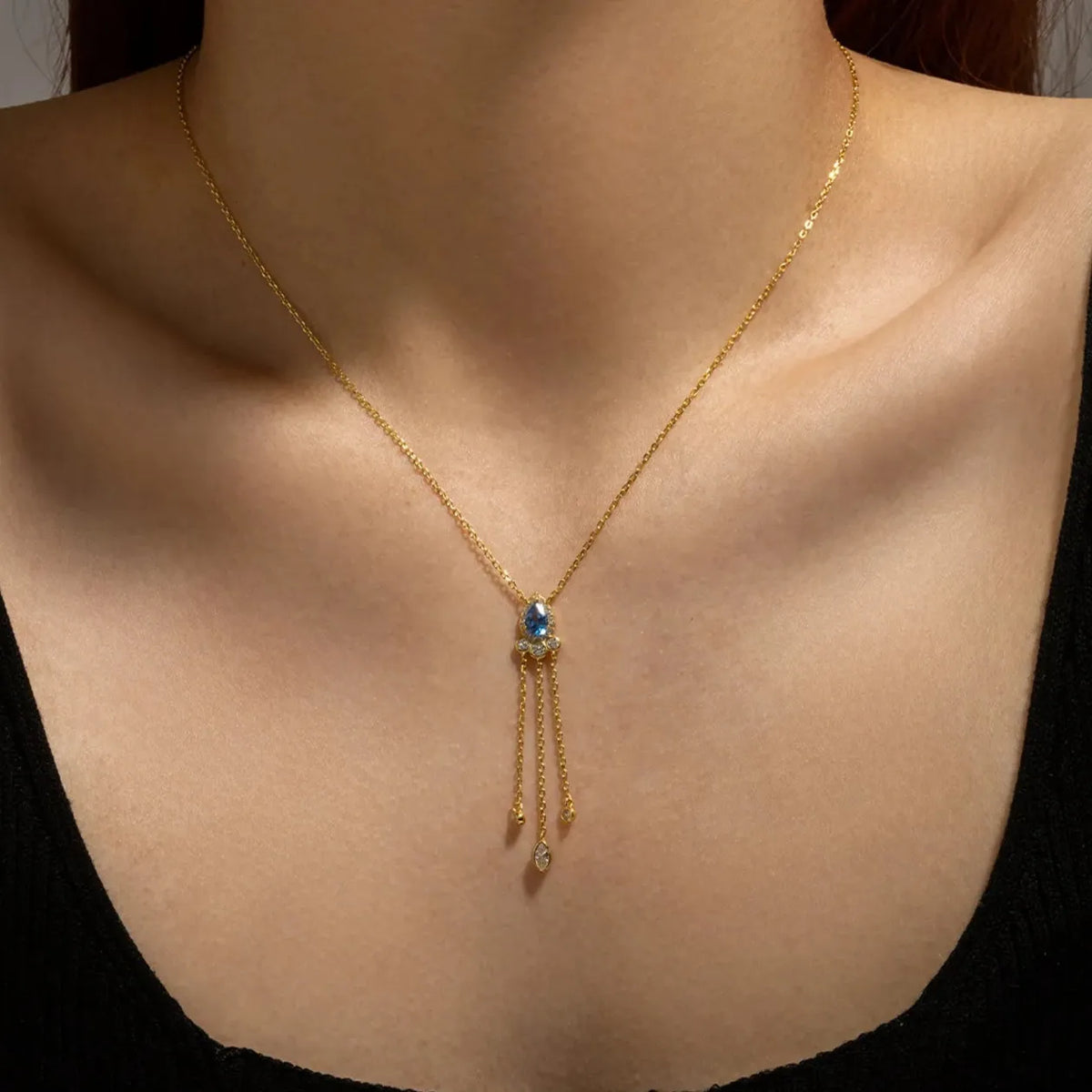 Woman wearing the Isabella radiant drop necklace in gold, blue stone with fine tassel chains