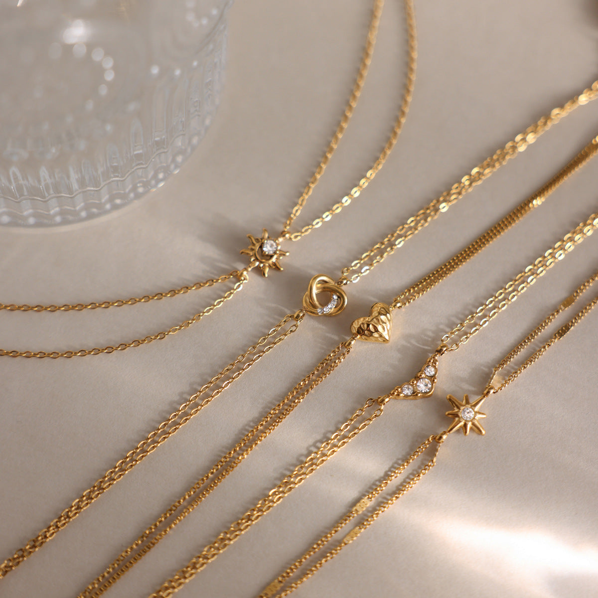 Inès crystal chevron bracelet among double chain charm bracelets on a satin surface