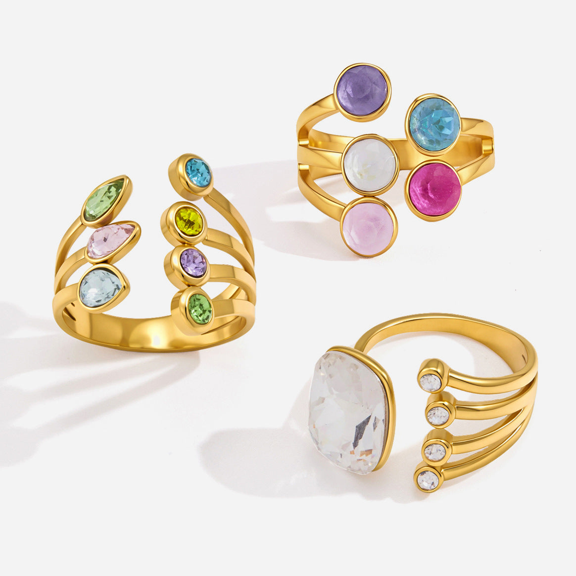 Three coloured-stone gold rings on white: the Isabella rainbow stone ring at the top right