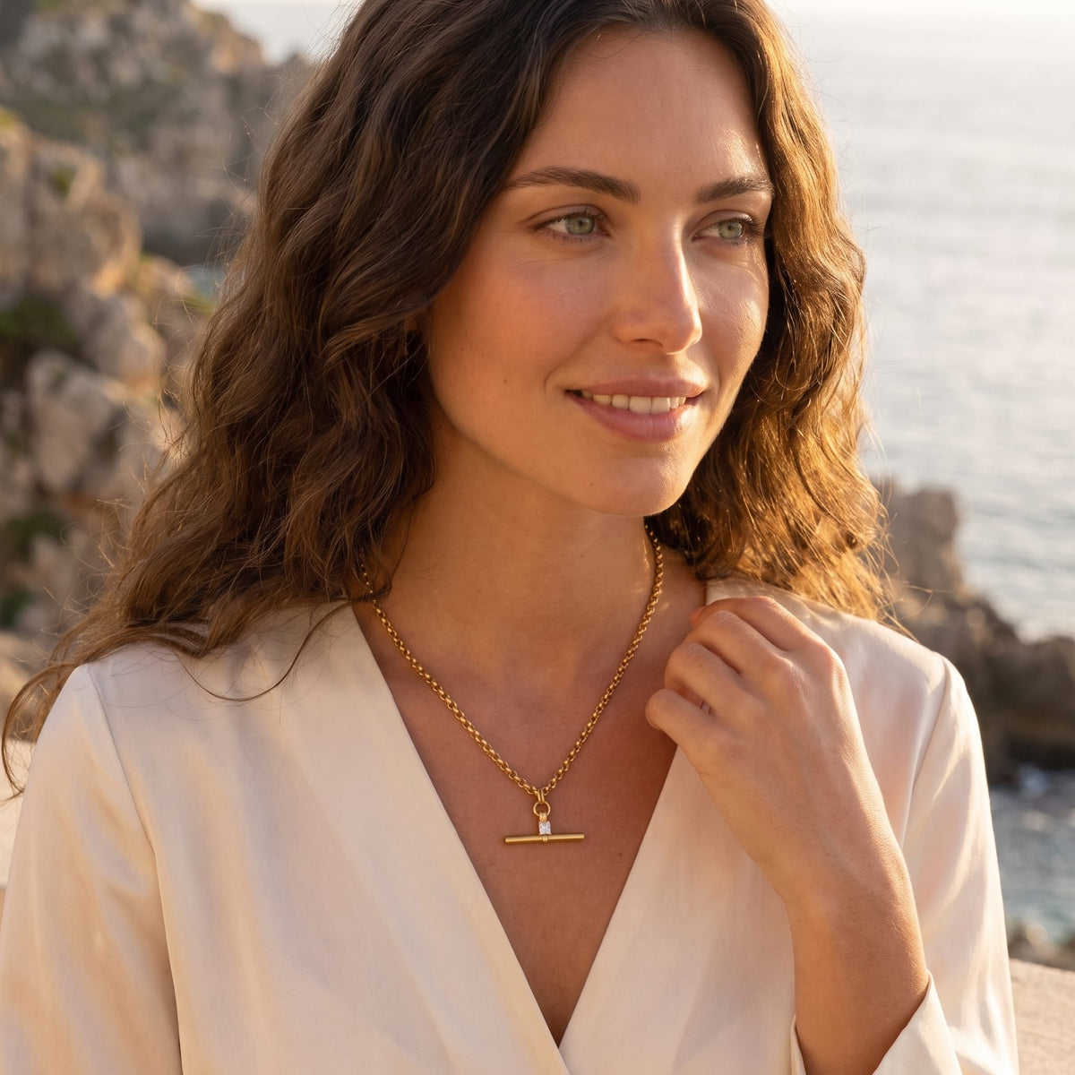Woman wearing the Joséphine t-bar crystal gold necklace at the collarbone outdoors near rocky cliffs