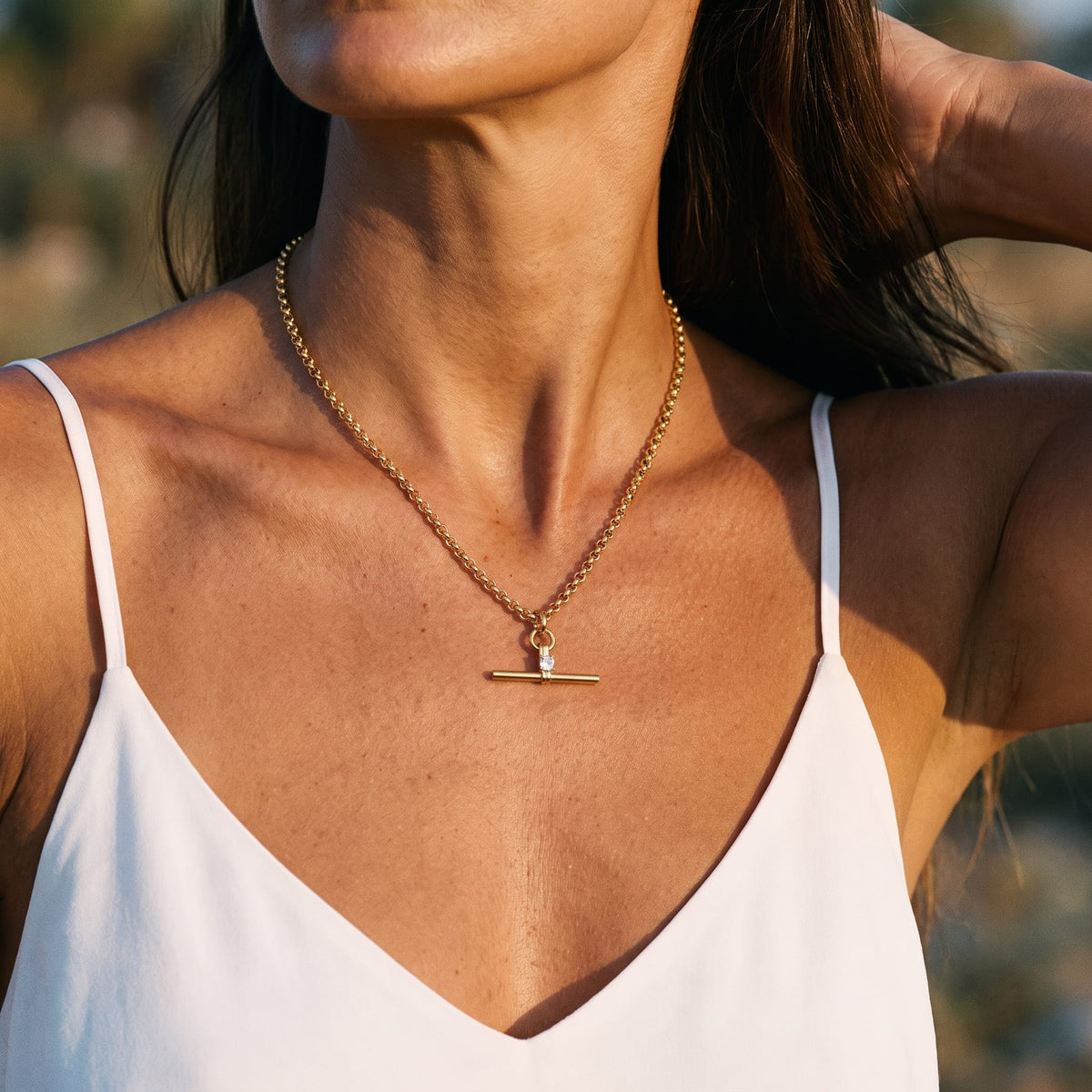 Woman wearing the Joséphine t-bar crystal gold necklace at the collarbone in a white camisole top