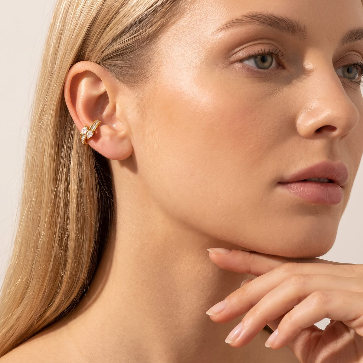Woman wearing the Laure baguette gold ear cuffs on her ear touching her chin