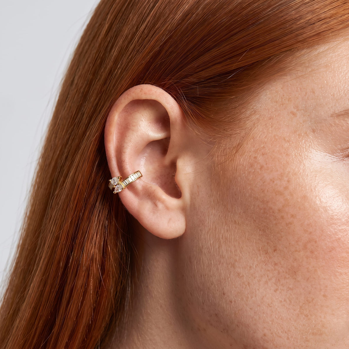 Wider view of a woman wearing the Laure baguette gold ear cuffs on her ear with red hair