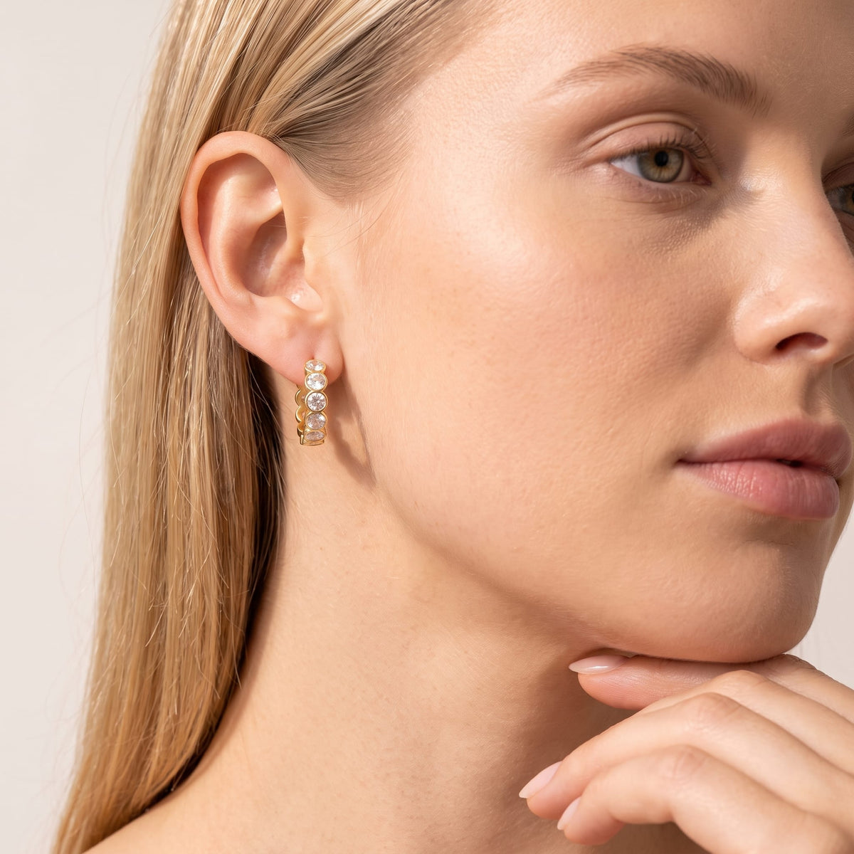Woman wearing the Léa bezel huggie gold earrings on the ear resting her chin on her hand