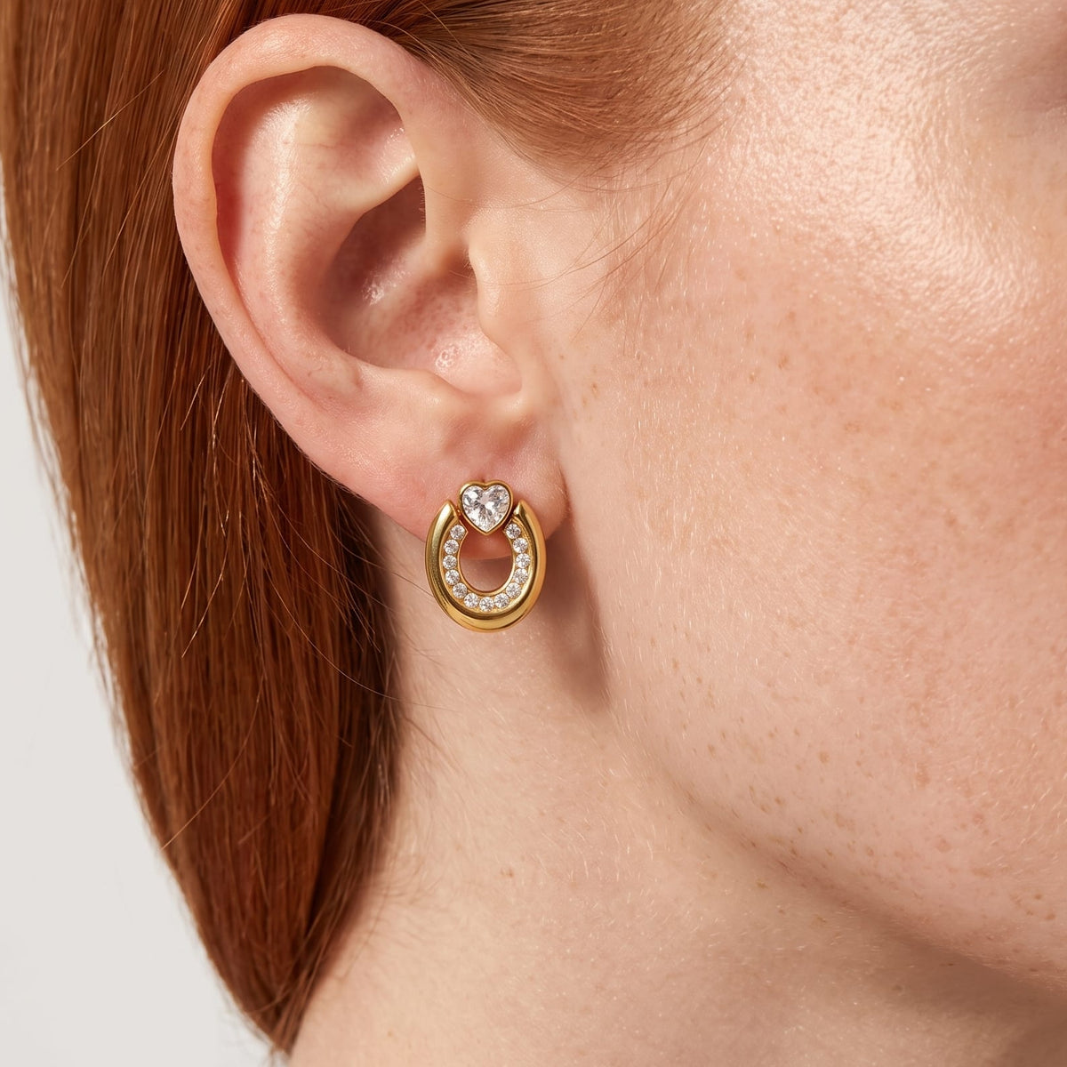 Woman wearing the Léonore horseshoe crystal gold earrings on her earlobe with red hair