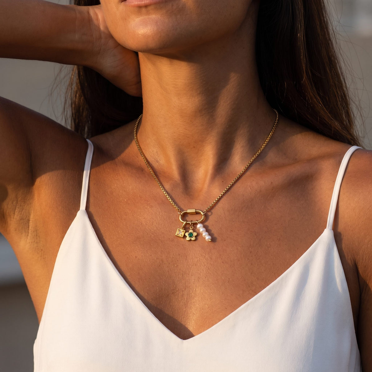 Woman in a white camisole wearing the Lilou daisy charm gold necklace in warm evening light