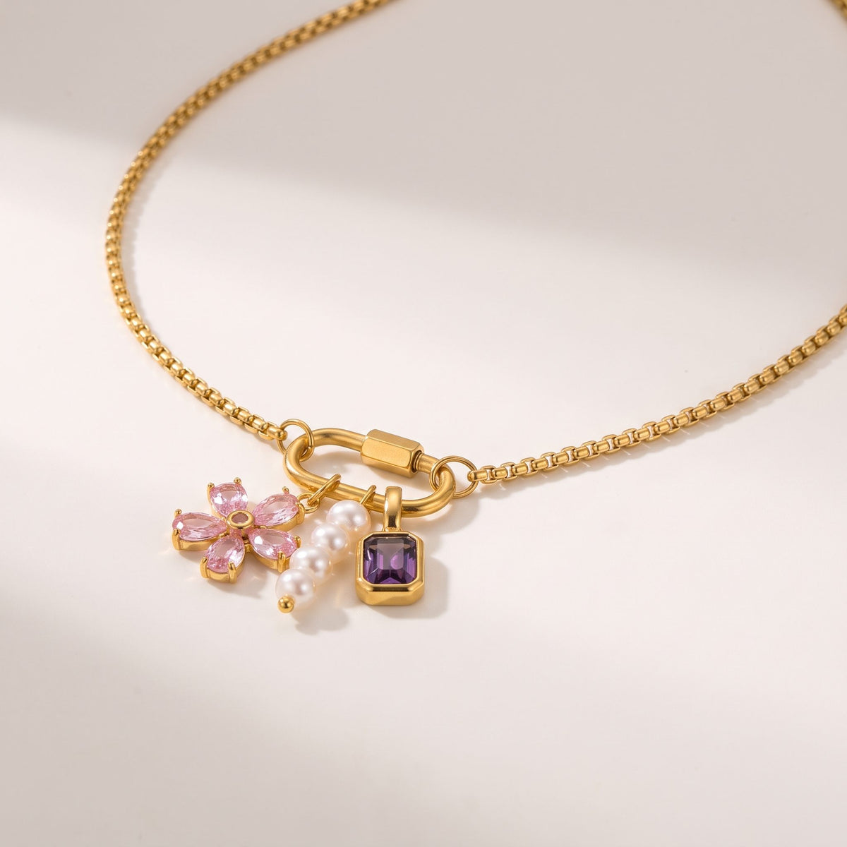 Close-up of the Lilou flower charm gold necklace on an off-white surface