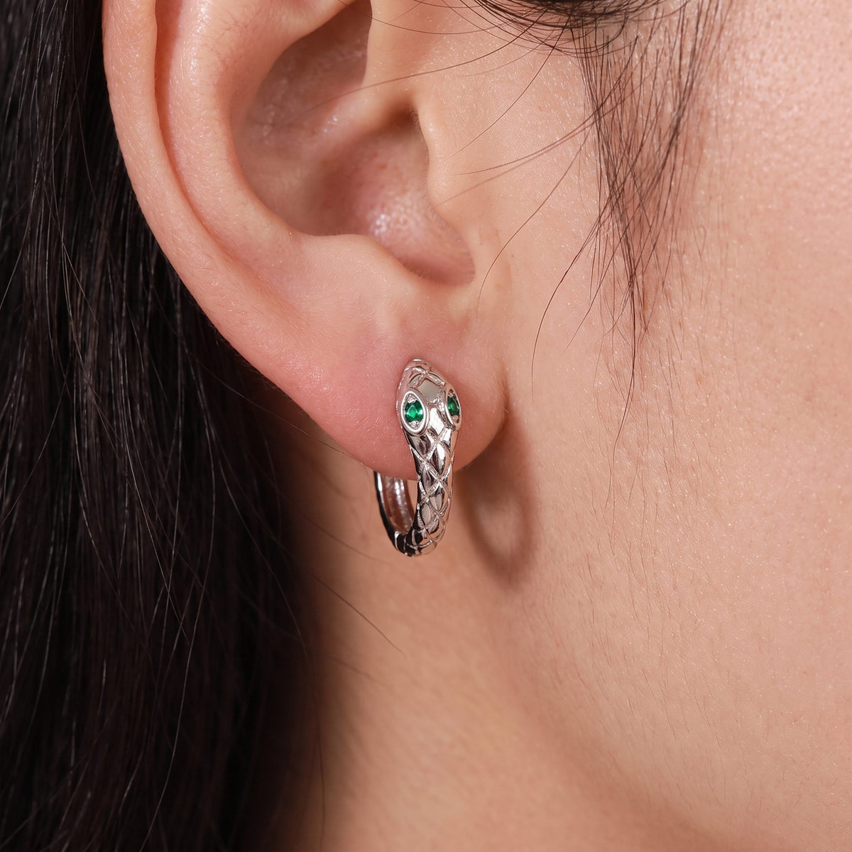 Woman wearing the Lilou silver snake hoop with a scaled texture and green crystal eyes