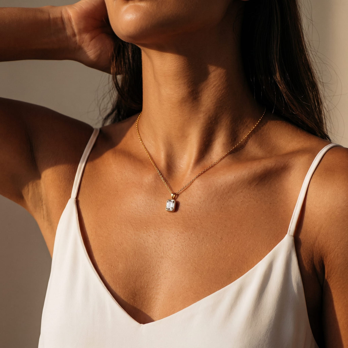Woman wearing the Livia emerald-cut solitaire gold necklace at the throat with warm indoor lighting