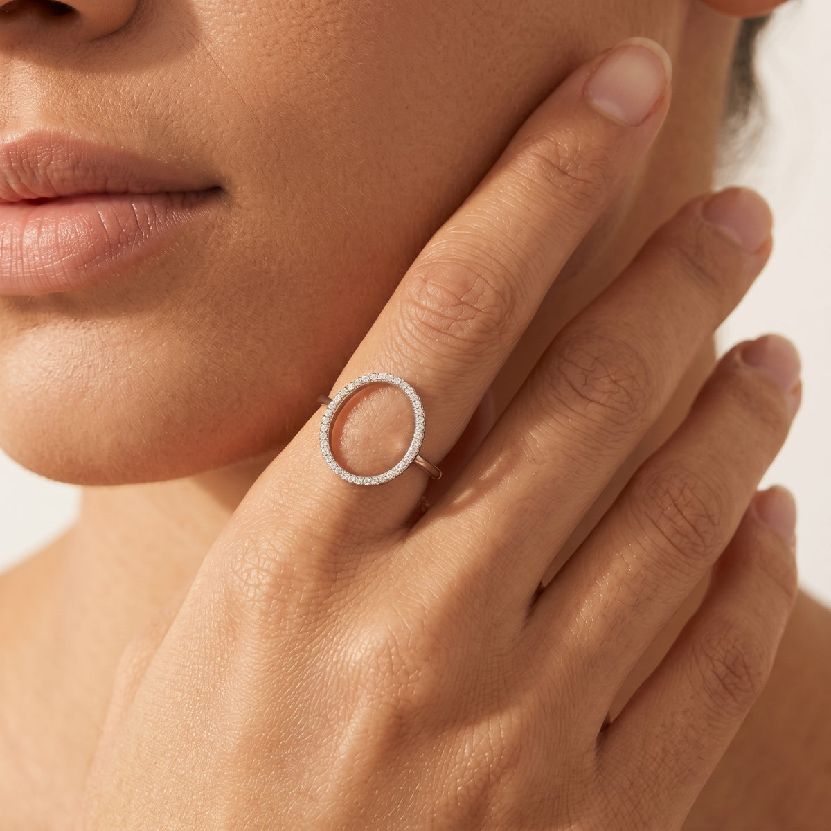 Hand at the jaw wearing the Luna silver circle ring, an open oval outlined in crystals