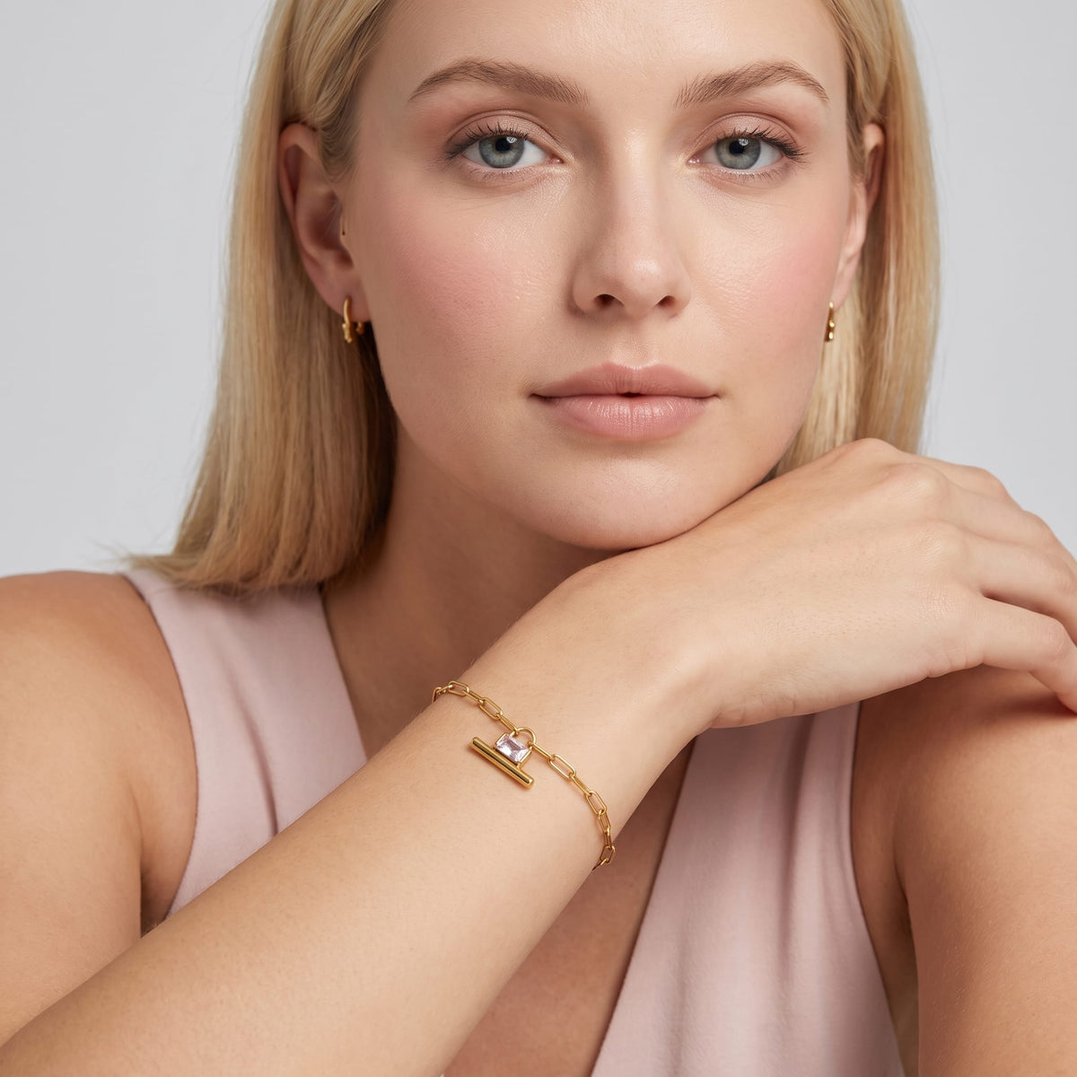 Woman wearing the Margaux padlock t-bar gold bracelet on her wrist resting under her chin