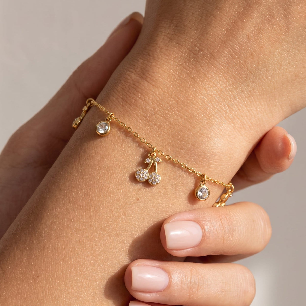 Woman wearing the Mélisa gold bracelet with a crystal cherry charm and round crystal drops on the wrist